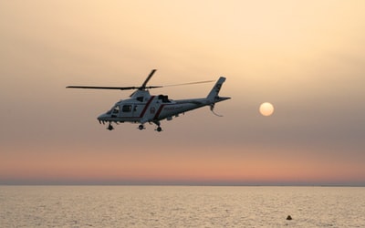 日落时白色和红色的直升机在海面上飞行